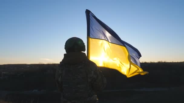 ウクライナ軍の女性は日没時に青黄色のバナーを振って丘のピークに立っている ウクライナの迷彩制服持ち上げフラグの若い女性兵士 ロシアの侵略概念への抵抗 — ストック動画