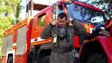 Oksijen maskesi takan üniformalı genç itfaiyeci itfaiye aracının yanında duruyor. Yangından sonra arka planda büyük kırmızı bir arabanın arka planına bakan erkek itfaiyeci portresi. Hayat kurtarma kavramı.