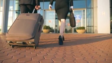 İş adamı ve Havaalanı Bagaj ile olacak kadın. Bavul tekerlekleri üzerinde taşıyan ve kadın meslektaşı ile terminal binasına yürüme genç iş adamı. Gezi veya seyahat kavramı ağır çekim