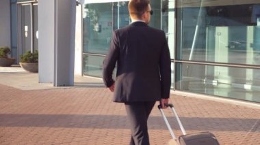 Terminalin yanında yürüyen ve tekerlekli bavulu çeken takım elbiseli başarılı bir iş adamı. Tanınmayan genç iş adamı bavuluyla havaalanına gidiyor. Yavaşça kapat..