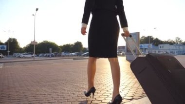 Havaalanından ya da bekleme odasından bavuluyla yürüyen bir iş kadını. Terminalden çıkıp tekerlekli bavula binen topuklu genç bir kız. İş kadını caddeye çıkıyor. Yavaş çekim.