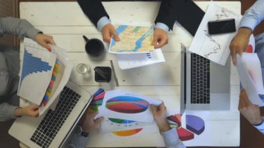 Hands business people sitting at table in trendy office and examining graphs. Group of busy employees working efficiently on business development. Creative team work indoor. Slow motion Top view
