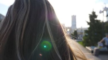 Kentsel cadde ve düzleştirme saç ayakta tanınmaz koyu saçlı kadın. Arka planda parlak güneş ışığı ile şehir ortamında ayakta kız. Bayan zevk esinti oynuyor ile onu saç.