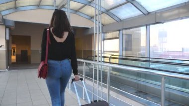 Yüksek topuklu ayakkabı giyen, tekerlekli bavulu yuvarlayan tanınmamış genç bir kız. İş kadını bavuluyla terminal koridorundan geçiyor. Bayan seyahate çıkıyor. Seyahat ya da iş seyahati kavramı. Yavaş çekim