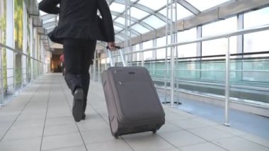 Bavullu tanınmayan iş adamı terminalin koridorunda koşuyor. Genç iş adamı uçağa geç kaldı. Takım elbiseli başarılı bir adam içeride koşuyor. İş gezisi için acele eden adam. Yavaş çekim.