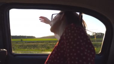 Eski arabanın camından sarkan ve rüzgarla oynayan mutlu kız. Yolculukta elini rüzgârda sallayan genç bir kadın. Rüzgarı hissetmek için eski arabanın camından dışarı bakan kadın turist. Yavaş çekim.