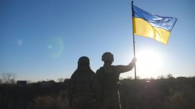 Ukrayna ordusunun kadın ve erkek askeri tepenin zirvesinde mavi-sarı pankartıyla dikiliyor. Askeri üniformalı genç kız ve adam Ukrayna bayrağını güneşli mavi gökyüzüne kaldırdı. Dolly vurdu..