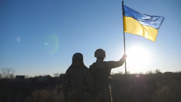 イギリス陸軍の女性兵士と男性兵士が 黄色の旗を掲げた丘の頂上に立っている 軍服を着た若い女の子と男は ウクライナの国旗を太陽とともに青空に向けて掲げた ドリー ショット — ストック動画