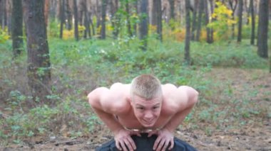 Ormanda şınav çeken güçlü bir adam. Erkek sporcu doğada egzersiz yapıyor. Genç adam dışarıda antrenman yapıyor. Kas sporcusu sıkı ve yoğun idman yapıyor. Spor anlayışı ve aktif yaşam tarzı. Kapat.