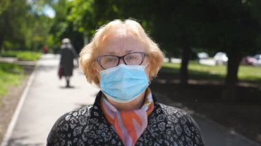 Tıbbi maskeli yaşlı kadın portresi şehir caddesinde duruyor. Büyükannem dışarıda COVID 19 virüsünden koruyucu maske takıyor. Koronavirüs salgınından sağIık ve güvenlik kavramı. Kapat.