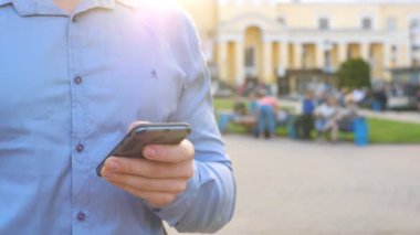 Başarılı bir iş adamı şehrin caddelerinde dikiliyor ve akıllı telefonlara bakıyor. Kendine güveni tam bir adam mesai arasında mesaj yazıyor ya da telefonunda uygulama kullanıyor. Arka plan bulanık. Ağır çekim. Yaklaş..