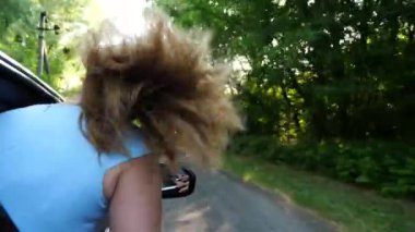 Sarı saçlı genç kız elini camdan dışarı çıkardı. Otomobil hareket ediyor ve gezinin tadını çıkarıyordu. Kaygısız kadın arabadan eğilir ve kır yolunda giderken kolunu uzatır. Yavaş çekim.