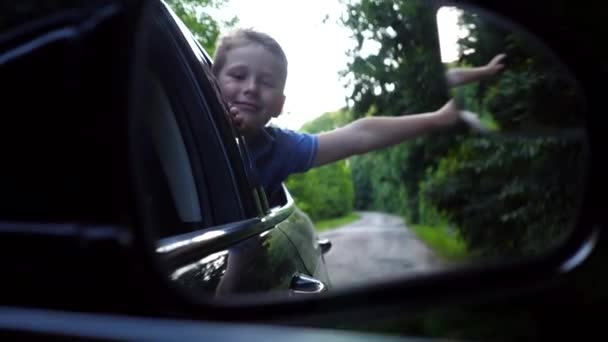 移動する車の横の鏡を反射する小さな少年 小さな子供が自動車窓から飛び出し 国道を走りながら手を握りました 車で運転しながら旅行を楽しんでいる子供 — ストック動画