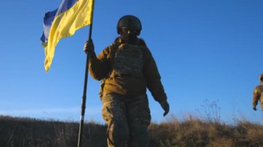 Soldiers of ukrainian army walks at field with flag of Ukraine. People in military uniform waving national yellow-blue flag as sign of victory against russian aggression. Invasion resistance concept.