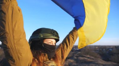 Ukrayna bayrağı sallayan Ukrayna ordusunun kadın askeri. Askeri üniformalı ve kasklı kız sarı-mavi bayrak kaldırdı. Rus saldırısına karşı zafer. İstila direnci konsepti. Yavaşla