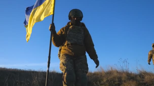 ウクライナ軍の兵士はウクライナの旗を掲げて戦場を歩く ロシアの侵略に対する勝利の印として 国の黄色の旗を振って軍の制服の人々 侵入抵抗概念 — ストック動画