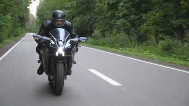 Kırsal Orman Yolu 'nda modern spor motosiklet süren kasklı genç bir adam. Motosikletli, tahta yolda motosikletiyle yarışıyor. Yolculuk sırasında bisiklet süren adam. Özgürlük ve macera kavramı. Ön görünüm.