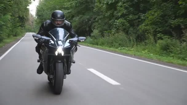 田舎の森の道路で現代のスポーツバイクに乗ってヘルメットで若い男 オートバイは木道でバイクを走らせている 旅行中にバイクを運転する男 自由と冒険の概念 正面図 — ストック動画