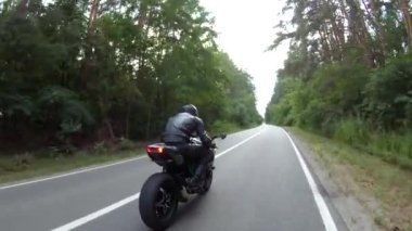 Orman yolundaki motosikletli motorcuları takip edin. Kasklı adam ormanın yakınındaki kırsal yolda modern spor motosiklet yarışı yapıyor. Yolculuk sırasında ya da yolculukta bisiklet süren adam. Özgürlük kavramı.