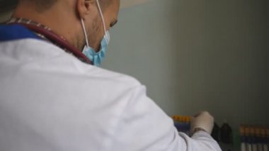 Doktor üniforma giyip test tüplerini kontrol ediyor. Doktor, COVID-19 'a analiz örnekleri inceliyor. Laboratuvarda çalışan bir bilim adamı. Korona virüsü salgınından korunmak için. Kapat..