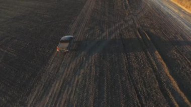 Aerial shot of pickup truck driving through plowed field after harvesting. Flying over car moving among farmland at autumn. Off road vehicle riding along ploughed meadow. Concept of agronomy farming.