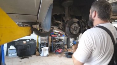 Profesyonel oto tamircisi atölyede vidaları özel elektrikli aletle söker. Garajda kaldırma aracıyla çalışan bir adam. Tamirci araba tamir ediyor. Otomobil bakımı kavramı. Yavaş çekim.