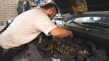 Tamirci atölyede ya da serviste anahtarı kullanarak arabanın motorunu tamir ediyor. Profesyonel oto tamircisi araç kaputu altında çalışır. Otomobil tamircisi garajda. Bakım ve tanı kavramı