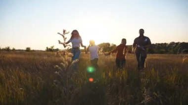 Çocukları olan mutlu ebeveynler gün batımında çimlerin üzerinde birbirlerinin kollarını tutarak koşuyorlar. Çocuklu genç bir aile birlikte çayırlarda koşmaktan hoşlanıyor. Aile mutluluğu kavramı