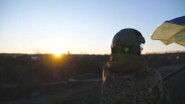 Askeri üniformalı genç bir kadının gün batımının arka planında mavi-sarı bayrak sallarken çekilen resmi. Ukraynalı kadın asker ulusal bayrağı kaldırıyor. Ukrayna topraklarının işgali kavramı