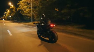 Motosikletli, akşam saatlerinde motosikletiyle yarışıyor. Şehrin gece caddesinde modern motosiklet süren bir adam. Yolculuk sırasında bisiklet süren adam. Özgürlük ve macera kavramı. Arka görünüm Kapat.