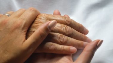Annesinin şefkatini ya da sevgisini gösteren elini nazikçe tutan ve okşayan bir kadın. Klinikte yatan yaşlı bir annenin kırışık kolunu rahatlatan kızı. Kız, eski ailesine destek oluyor. Üst görünüm.