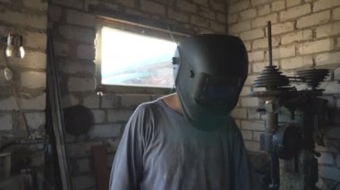 Erkek kaynakçı atölyede çalışmak için koruyucu maskeyi indiriyor. Eldivenli tamirci lehimleme demiri alıyor ve metal parçaları garajda kaynak yapmaya hazırlanıyor. Bakım hizmeti kavramı. Kapat..