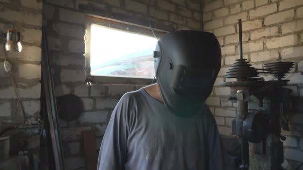 ワークショップで働くために保護マスクを下げる男性の歓迎 はんだ付けされた鉄を取る手袋の修理人およびガレージの金属の部品を溶接する準備 保守サービスのコンセプト クローズアップ — ストック動画