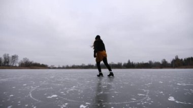 Genç sporcu kadın kışın buz nehrinde kayan artistik patenlerle nallandı. Donmuş günde gölde kadın patenci pratik yapıyor. Kız spordan hoşlanıyor ve soğuk havada aktif boş vakit geçiriyor. Yavaş çekim.