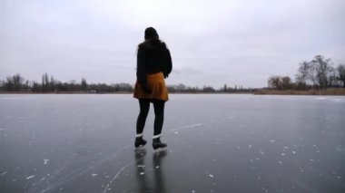 Bulutlu bir günde buz yüzeyinde buz pateni yapan kadın patenci. Sporcu kadın, donmuş nehir ya da gölde artistik patinaj eğitimi almış. Kadın becerilerini geliştiriyor ve kış soğuğunda aktif boş vakitleri oluyor. Yavaş çekim