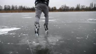Dışarıdaki buz yüzeyinde kayan artistik patenli genç adam. Bulutlu bir günde donmuş nehirde kayan adam. Sporcu sporu seviyor ve kış aylarında aktif boş vakitleri oluyor. Yavaş çekim.