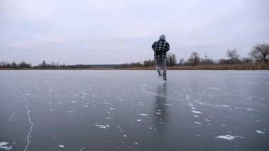 Bulutlu bir günde donmuş nehirde kayan adam. Dışarıdaki buz yüzeyinde kayan artistik patenli genç adam. Soğuk kış havasında gölde sporcu eğitimi. Kış zamanı aktif bir eğlence. Yavaş çekim.