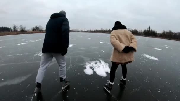 若い男性と女性は 屋外のアイスリンクにスライドフィギュアスケートで揺れています 曇りの冬の日に凍った川でスケートすることを学ぶ友人 アクティブなレジャー 健康的なライフスタイルの概念 スローモーション — ストック動画