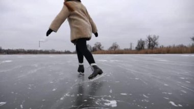 Kürk mantolu genç kadın donmuş nehirde rotasyon eğitimi alıyor. Buz pateni pistinde kayan artistik patenli bir kız. Sporcu kadın soğuk havada gölde paten kayıyor. Kış mevsiminde aktif boş zaman.