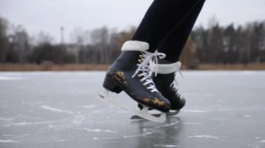 Kadın bacakları doğada buz yüzeyinde kayan artistik patenlerle nallandı. Donmuş nehirde buz patenci kadın ayakları. Sporcu kadın, soğuk havada gölde becerilerini geliştiriyor. Kışın aktif eğlence..