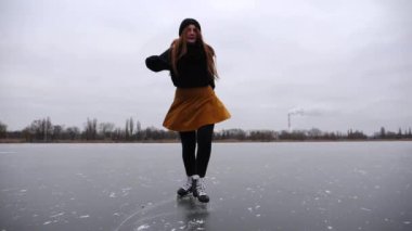 Buz yüzeyinde geriye doğru kayan artistik patenci kadın. Genç kız bulutlu bir günde donmuş nehirde paten kayıyor. Soğuk havada gölde pratik yapan bir kadın. Kış mevsiminde aktif boş zaman.