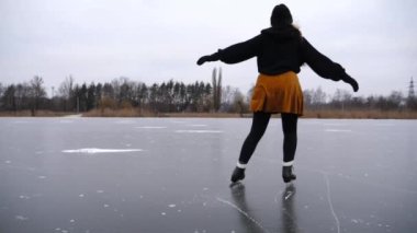 Genç kız donmuş nehirde rotasyon eğitimi alıyor. Buz pateni pistinde kayan artistik patenli bir kadın. Sporcu kadın soğuk havada gölette paten kayıyor. Kış günü boş vakit. Yavaş çekim.