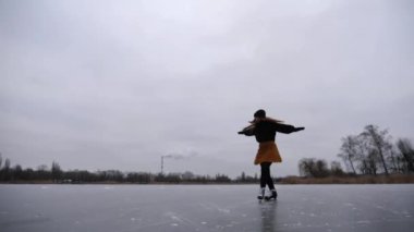 Dişi patenci dışarıda eğitim yaparken buz pateni pistinde düşüyor. Genç sporcu kadın donmuş nehirde artistik patenlerle pratik yapıyordu. Dondurucu kış gününde aktif eğlence. Yavaş çekim.