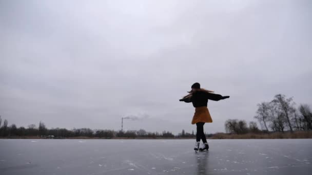 屋外で回転スキルをトレーニングしながらアイスリンクに落ちる女性スケーター 凍った川で練習するフィギュアスケートの若いスポーツウーマン 寒い冬の日にアクティブなレジャー スローモーション — ストック動画