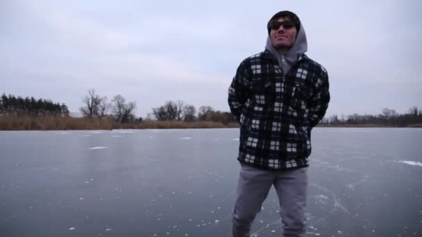 曇りの日に凍った川でスケートする男 若い男は 屋外の氷の表面に滑るフィギュアスケートで光っている 冬の寒さの中で湖でアクティブなレジャーをしているスポーツマン スローモーションを閉じる — ストック動画
