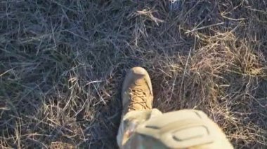 Ukraynalı kadın askerlerin kırsal alandaki kuru çimlerin arasından kahverengi çizmelerle geçmesine bakış açısı. Askeri ayakkabılı genç asker kız bacakları ekilmemiş tarlalarda yürüyor. Ukrayna 'da Savaş.