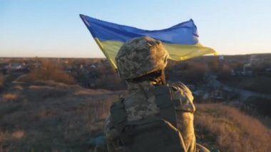 Ukraynalı askerin ulusal bayrağı kaldırdığı bir resim. Askeri üniformalı genç adam mavi gökyüzüne karşı Ukrayna bayrağı sallıyor. Savaşta zafer. Rus istilasına karşı direniş