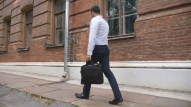 Evrak çantalı genç işadamı şehir caddesinde yürüyor ve telefonla konuşuyor. Kendine güveni tam bir adamın iş görüşmesi var. Ofis çalışanı finans merkezine koşuyor. Yavaş çekim.