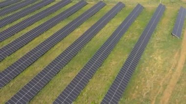 Yeşil alandaki güneş panelleri boyunca uçmak. Güneş enerjisi santrali elektrik üretir. Elektrik üreten güneş çiftliğinin hava görüntüsü. Ekoloji ve yenilenebilir yeşil enerji kavramı. Üst görünüm.