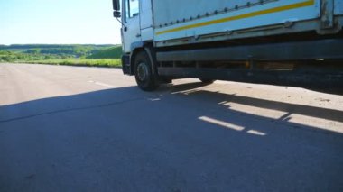Boş otoban boyunca giden ve malları taşıyan kargo karavanı olan kamyonun yan görüntüsü. Kamyon kırsal yoldan geçerek hedefe gidiyor. Kargo taşıma konsepti. Yavaş çekim.